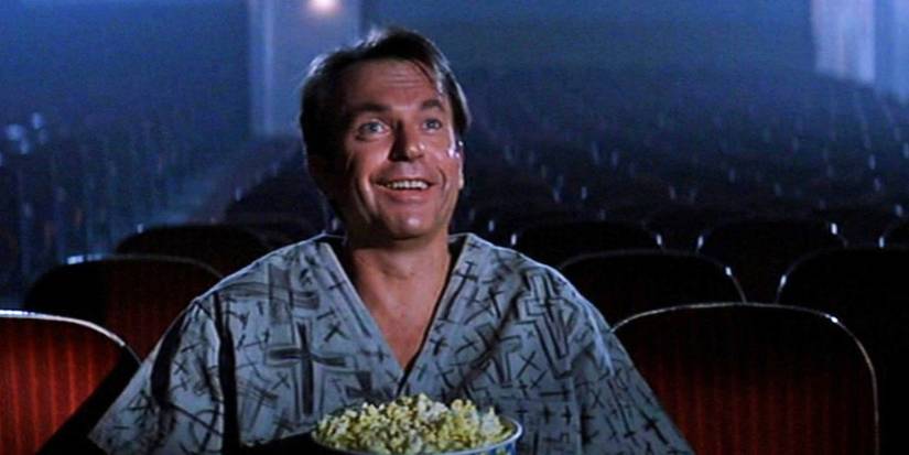 John Trent smiles while watching a movie at a theater in In the Mouth of Madness.