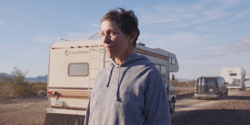 Fern standing on the side as a caravan of vans drive by in Nomadland
