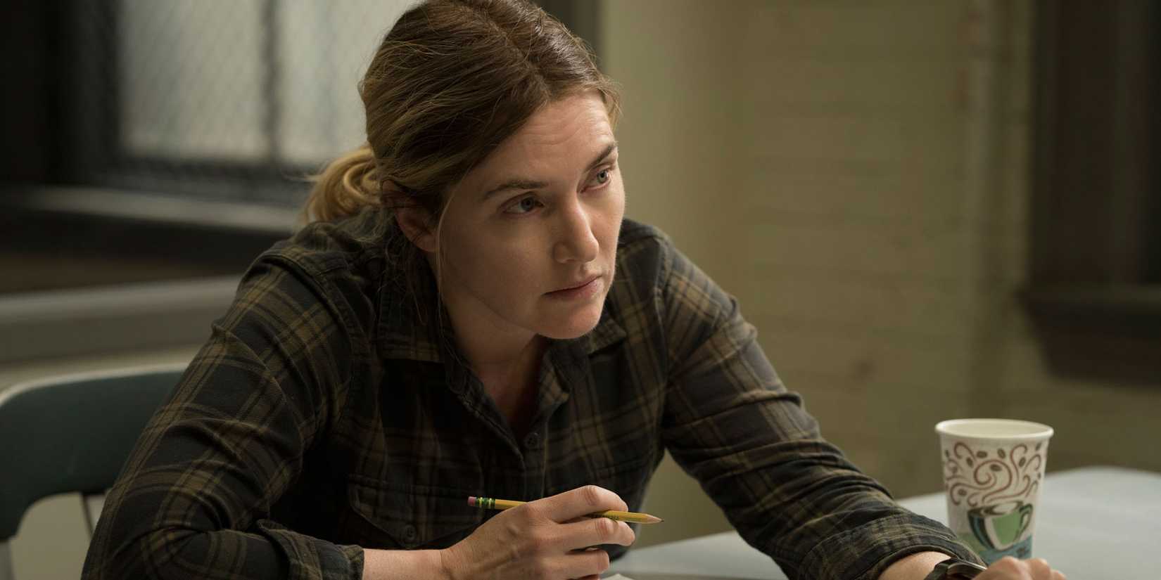 Mare Sheehan sitting down and looking intently at someone off-camera in Mare of Easttown.