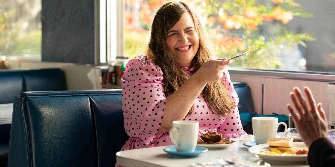 Annie smiling at a restaurant while chatting with someone off-camera in Shrill