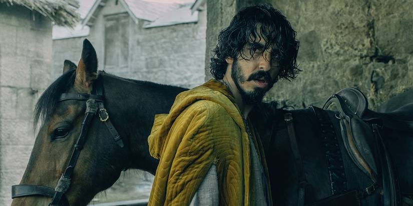 Dev Patel next to a horse with a yellow robe in 'The Green Knight'