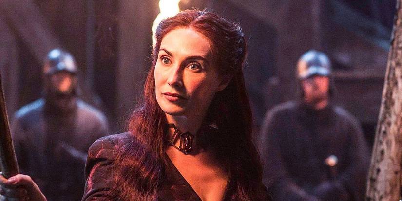 Carice van Houten as Melisandre holding a torch and looking curious in Game of Thrones.