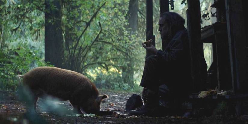 Nicolas Cage sitting on a porch with his pig eating before him in Pig