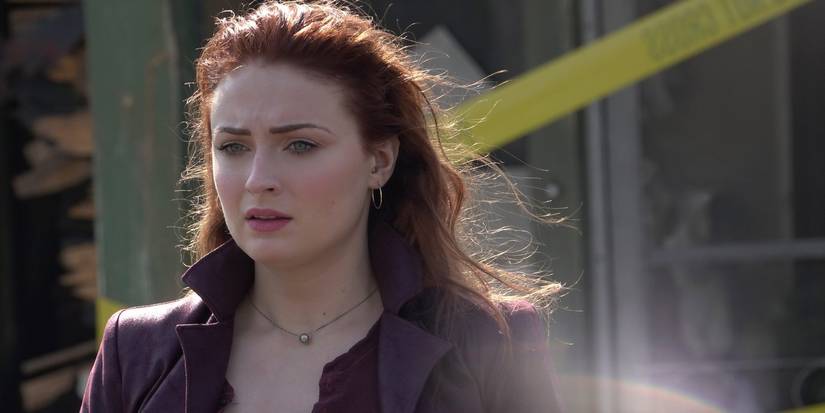 Sophie Turner as Jean Grey, wears a burgundy jacket & looks sadly at something offscreen in Dark Phoenix