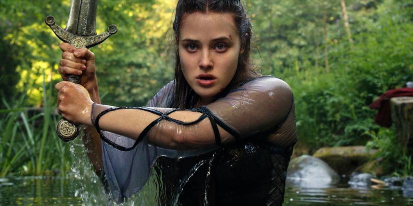 Nimue (Katherine Langford) coming out of a lake holding a sword in the show Cursed.