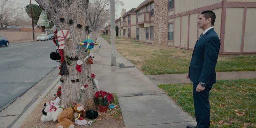 A man in a suit and tie stares at a tree covered with stuffed animals and remembrances in The Trials of Gabriel Fernandez.