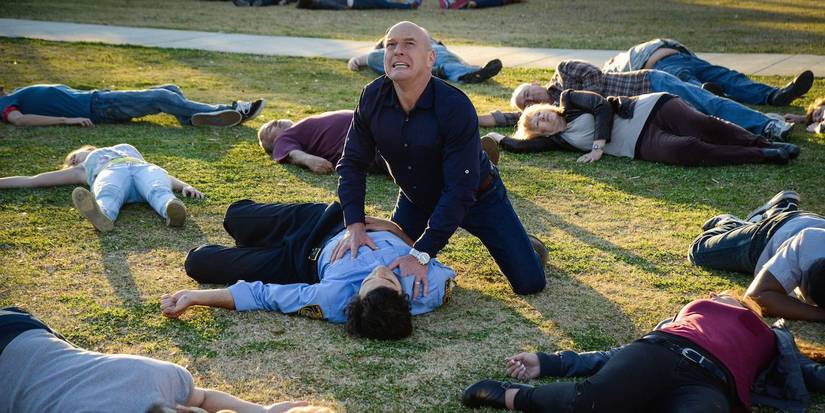 Dean Norris looking at the sky in agony as he's surrounded by bodies on the grass in 'Under the Dome'.