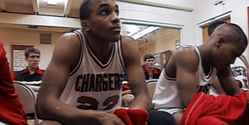 Basketball players wear team uniforms and sit in chairs looking tense in Hoop Dreams.