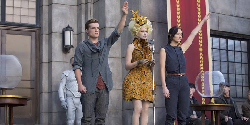 Peeta and Katniss doing the Mockingjay symbol while Effie stands between them