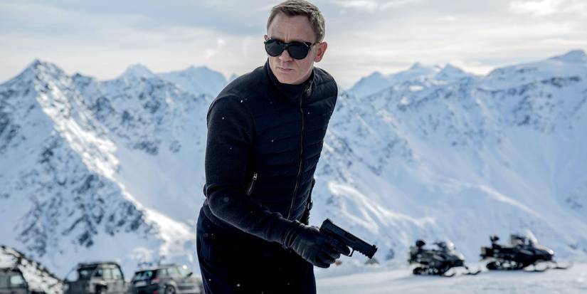 Daniel Craig as James Bond dressed in black holding a gun atop a snowy mountain in Spectre.