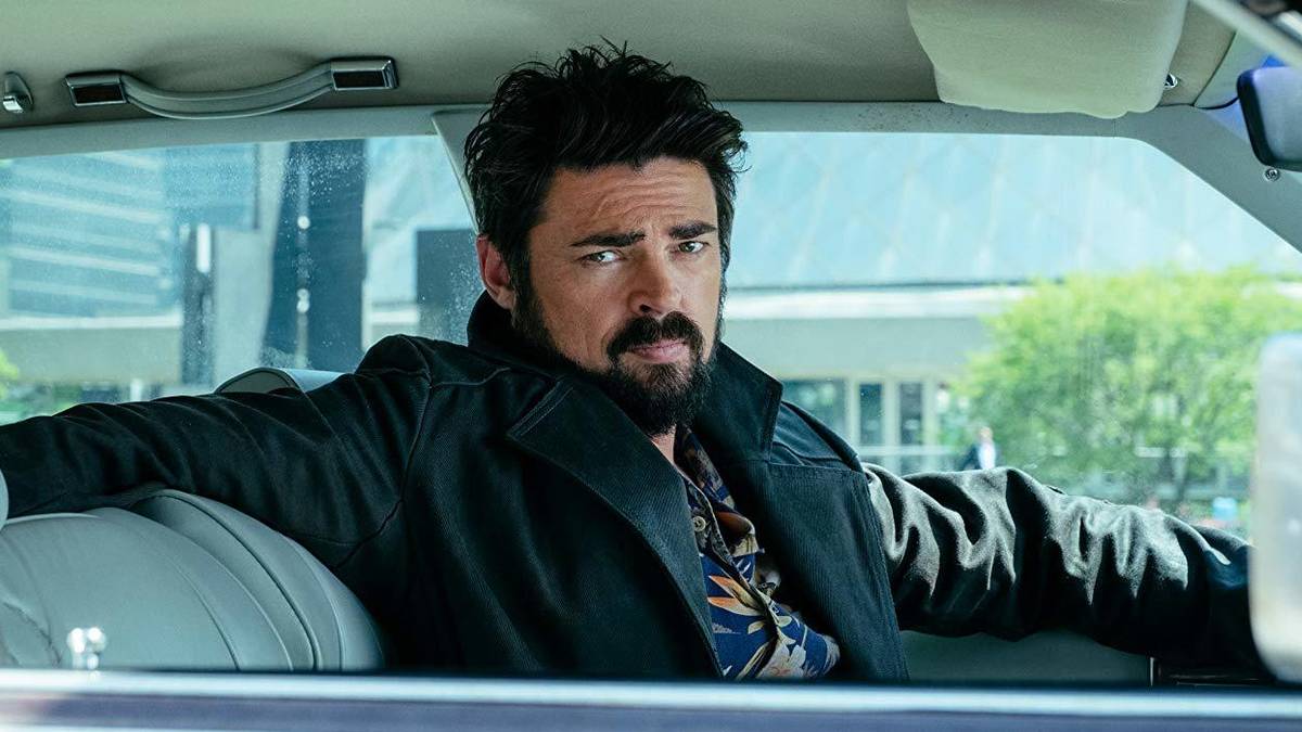 Karl Urban as Billy Butcher sits in a car, leaning back with his arm over the chair in The Boys.