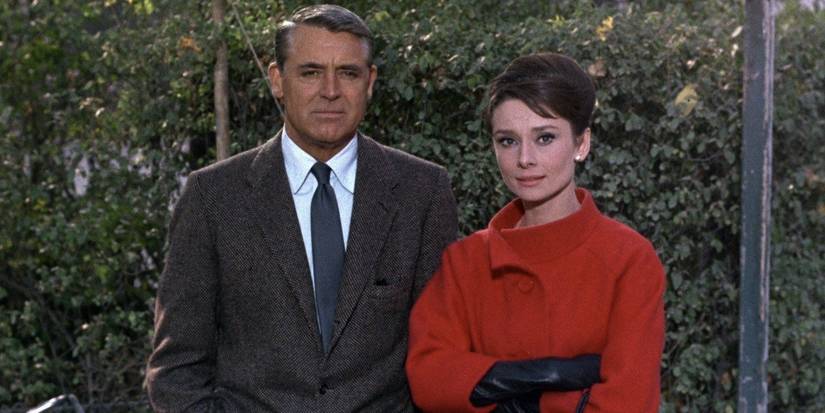 Audrey Hepburn wearing red standing next to Cary Grant in a suit in Charade
