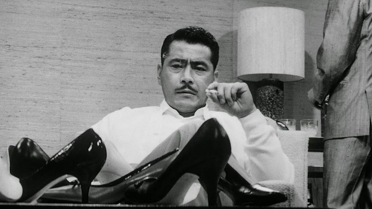 Toshiro Mifune as Kingo Gondo smoking a cigarette and staring at shoes kept on the table in High and Low.