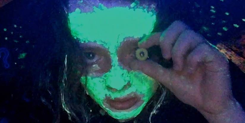 Anna Cobb wearing glow in the dark paint and holding a glass eye over her own.