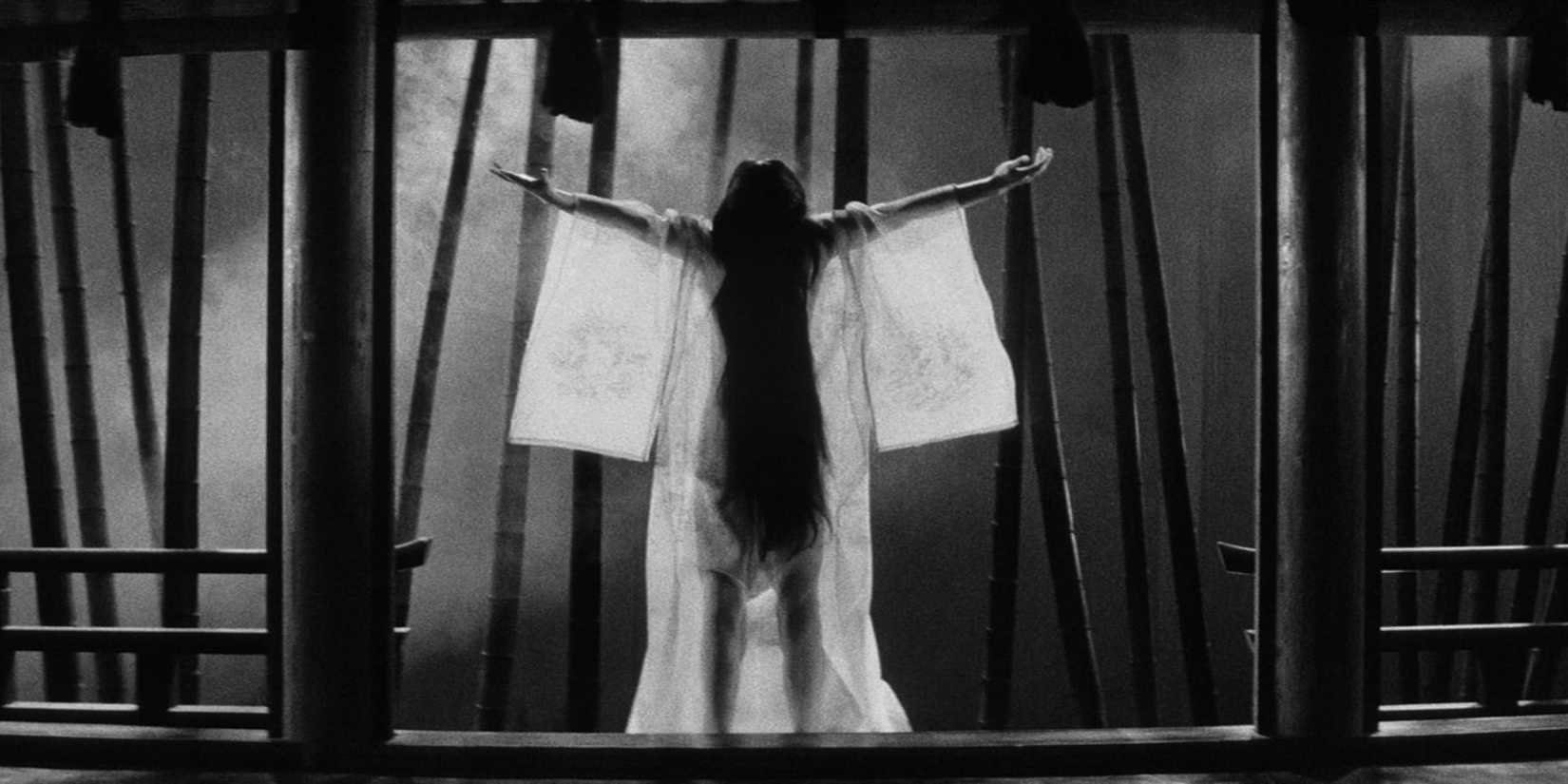 A woman spreading her arms in front of a window at night in Kuroneko 1968