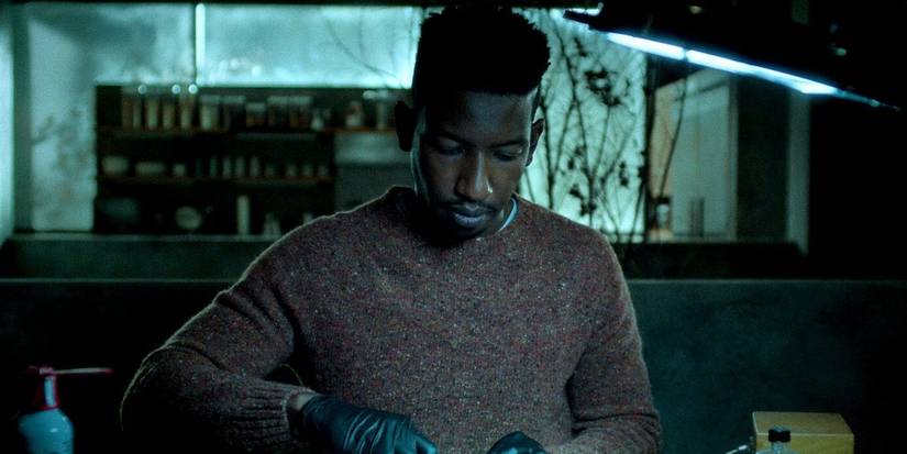 A person in Archive 81 with eerie lighting, wearing gloves, and gazing downwards while cutting something.