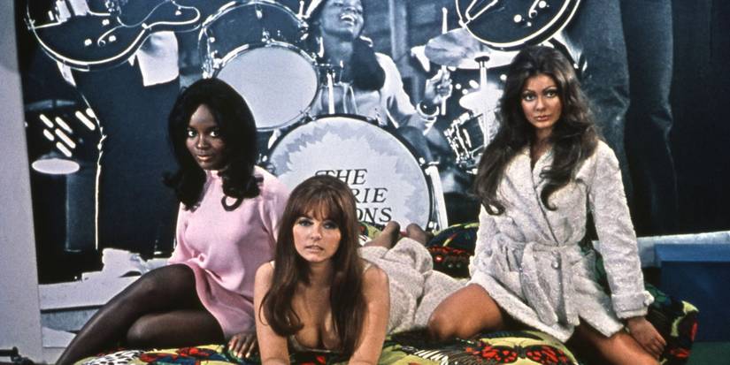 The cast of Beyond the Valley of the Dolls posing in bed.