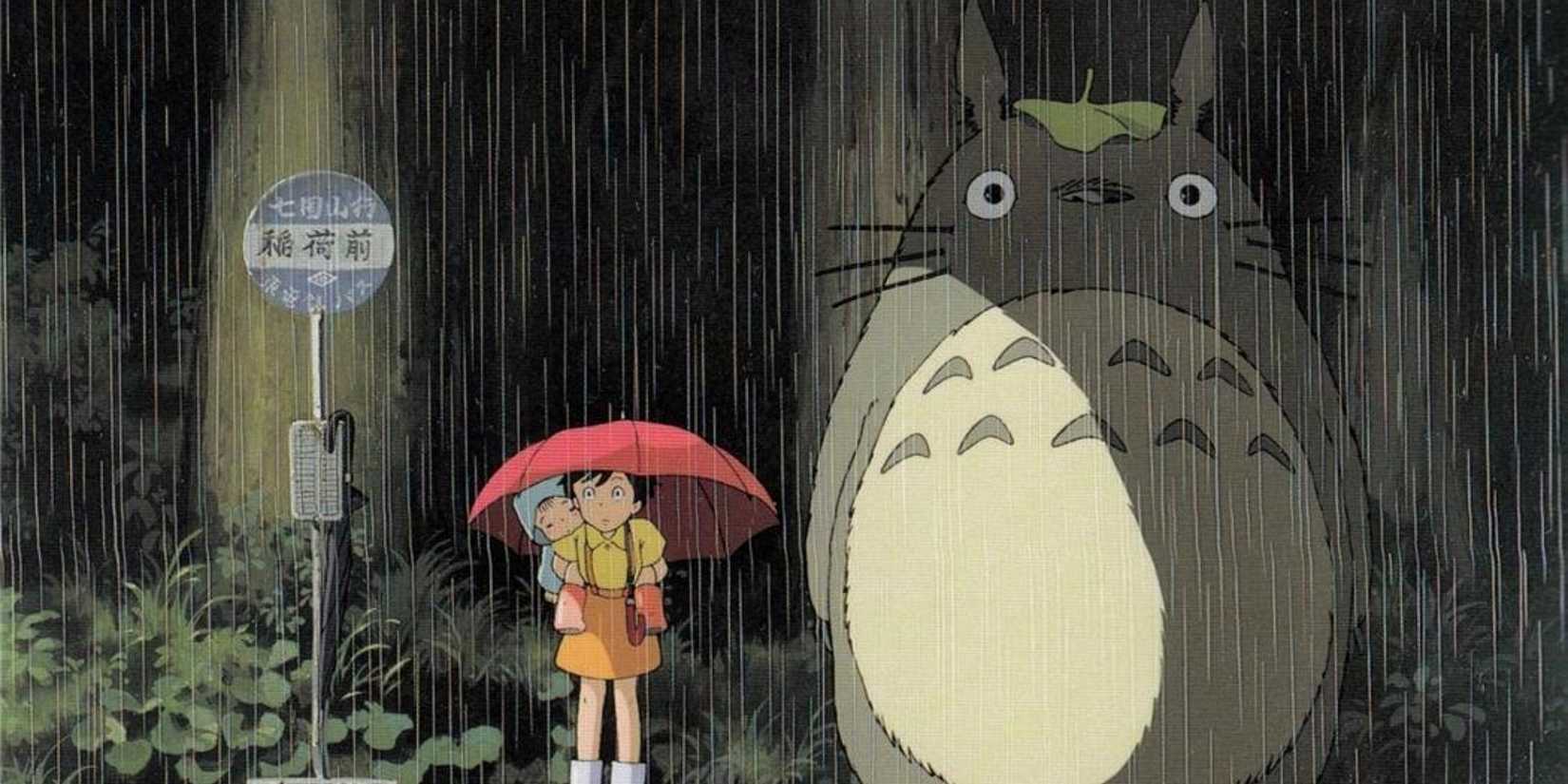 A girl under an umbrella stands next to Totoro in the rain at a bus stop in Studio Ghibli's My Neighbor Totoro.