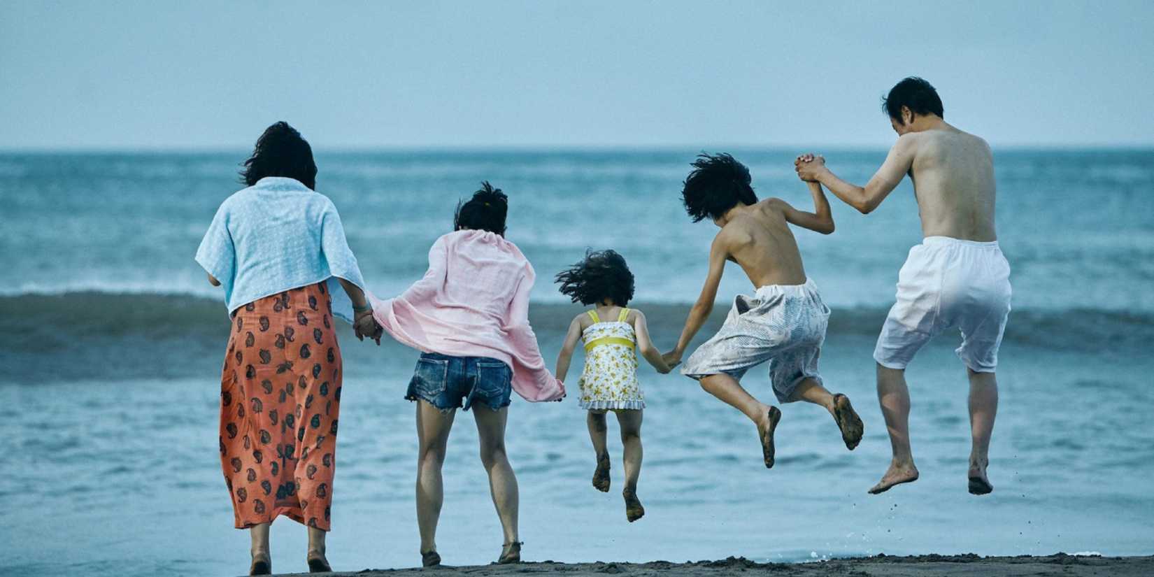 The family in Shoplifters jumping together and holding hands at the beach 