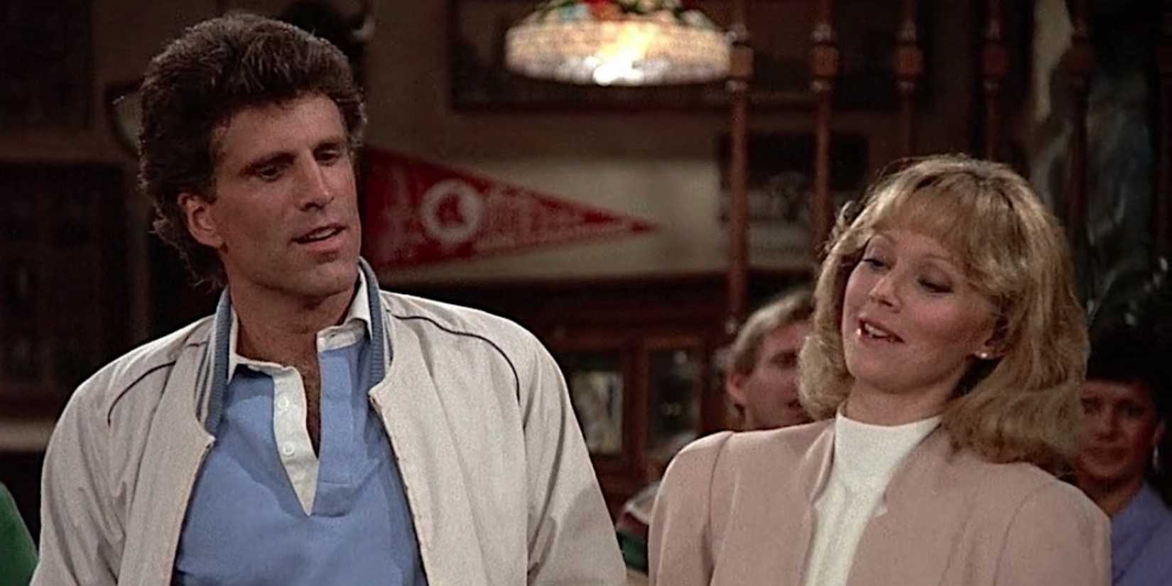 Ted Danson and Shelley Long stand next to each other with amused expressions in the bar in Cheers.