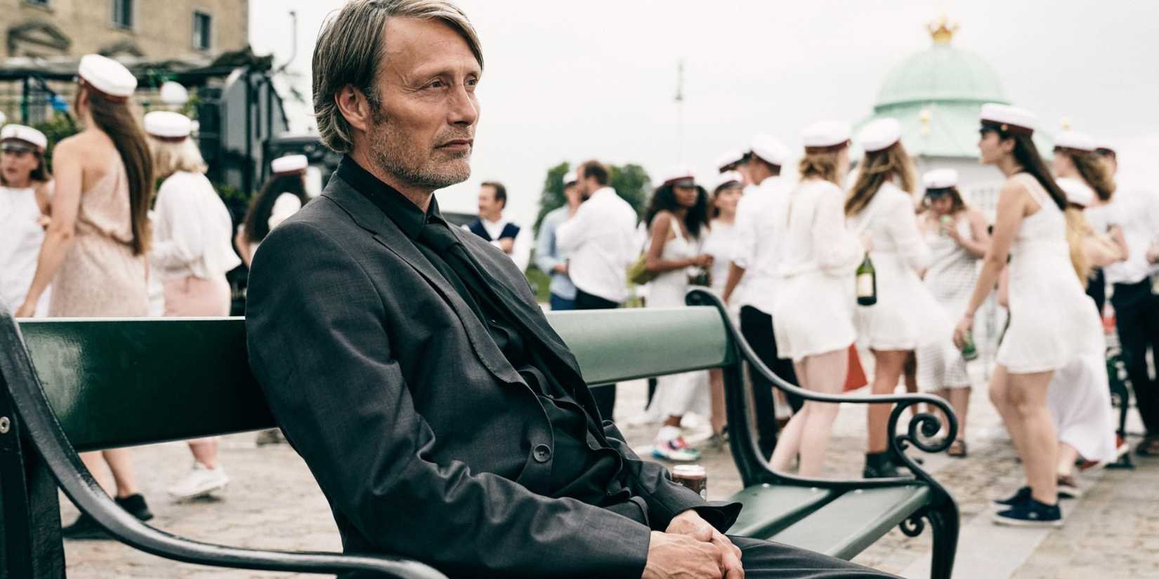 Mads Mikkelsen as Martin sitting on a bench looking pensive in Another Round (2020)