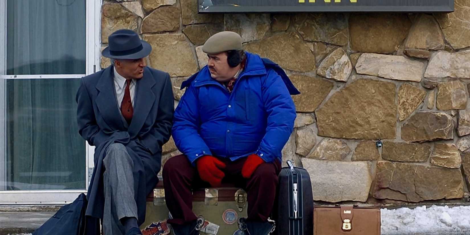 Neal and Del sit on their suitcases outside a building and talk in Planes, Trains and Automobiles.