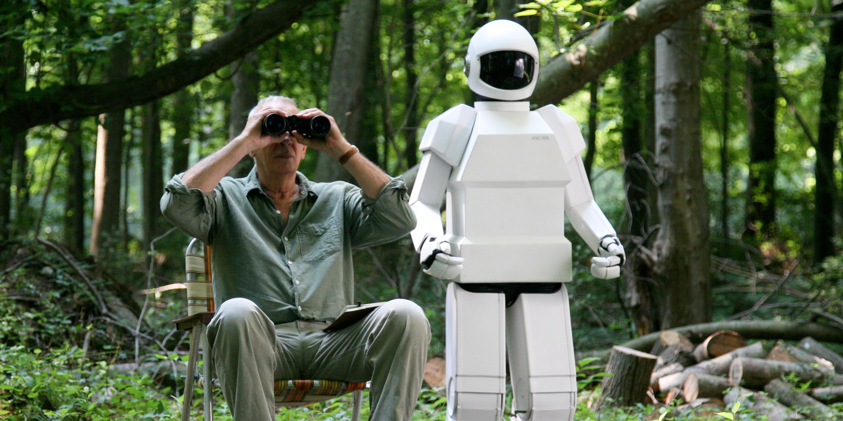 Robot And Frank in the woods as Frank uses a pair of binoculars 