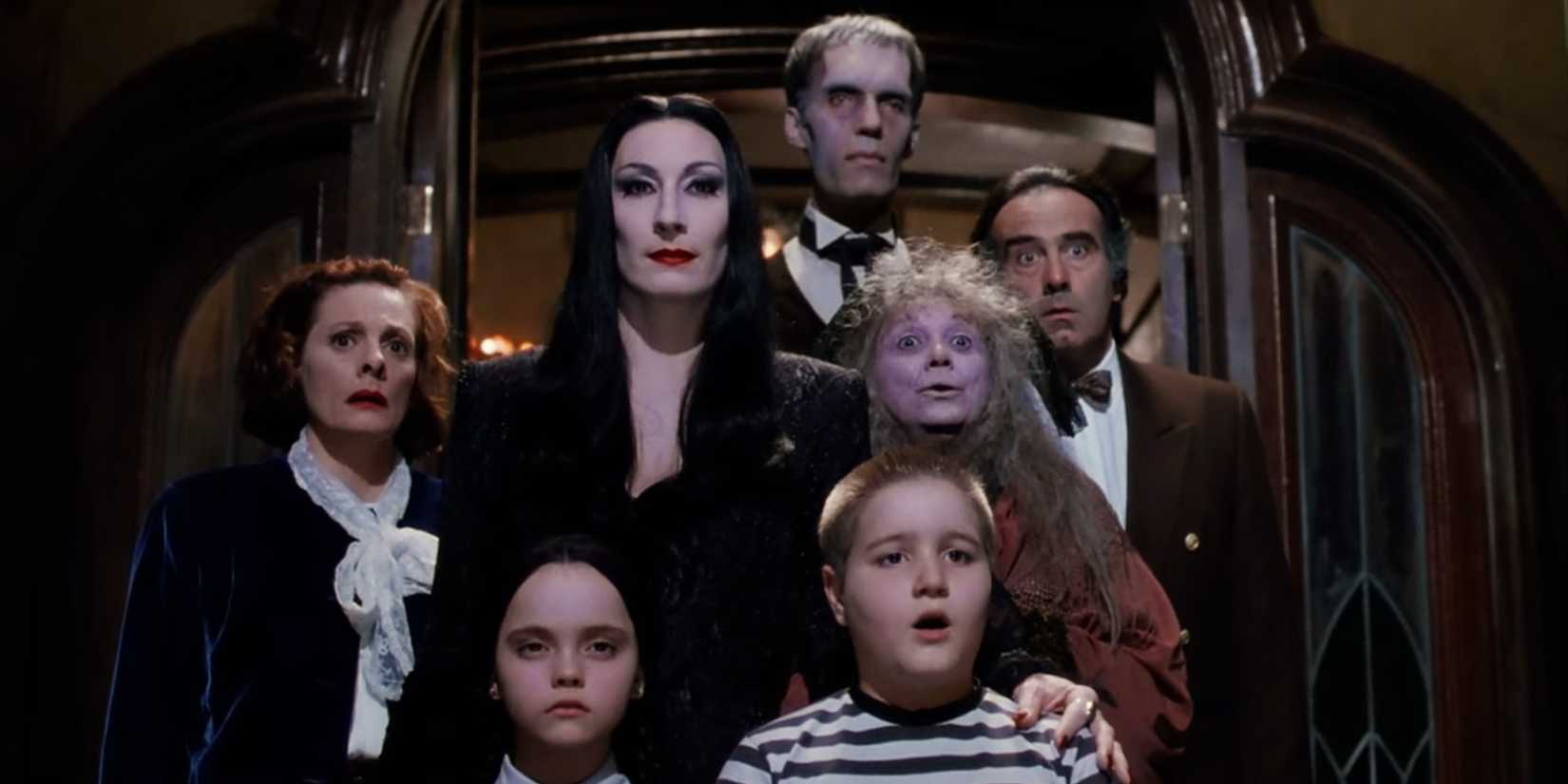 The cast stand in a doorway, some looking shocked in The Addams Family.