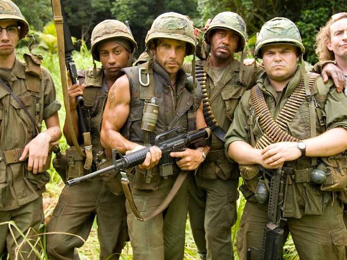 The cast of Tropic Thunder in soldiers' uniforms pose with weapons and look at the camera dramatically.