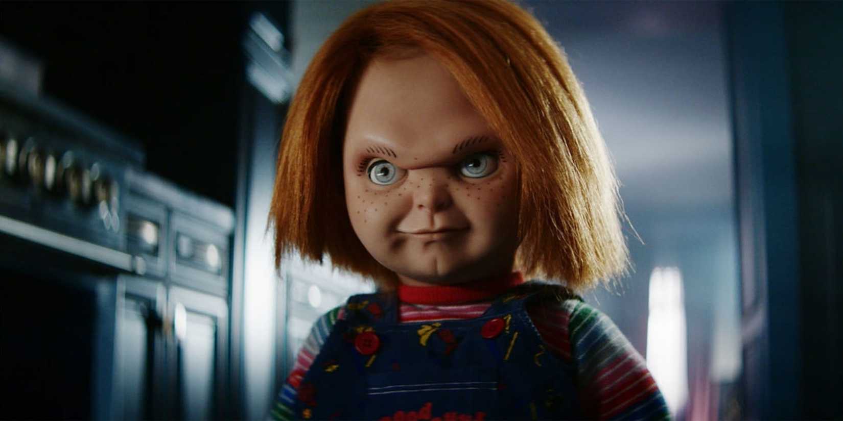 The doll Chucky stands in a dimly lit kitchen with a sinister look on its face in the Chucky TV series.