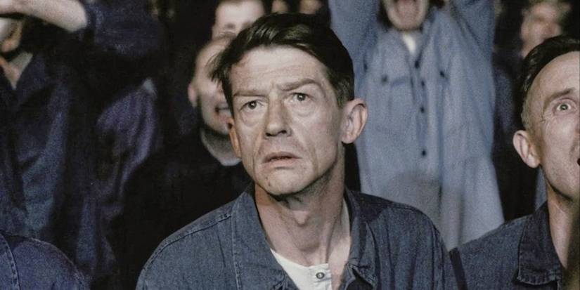 John Hurt looks concerned, standing in a crowd with others in "1984". 