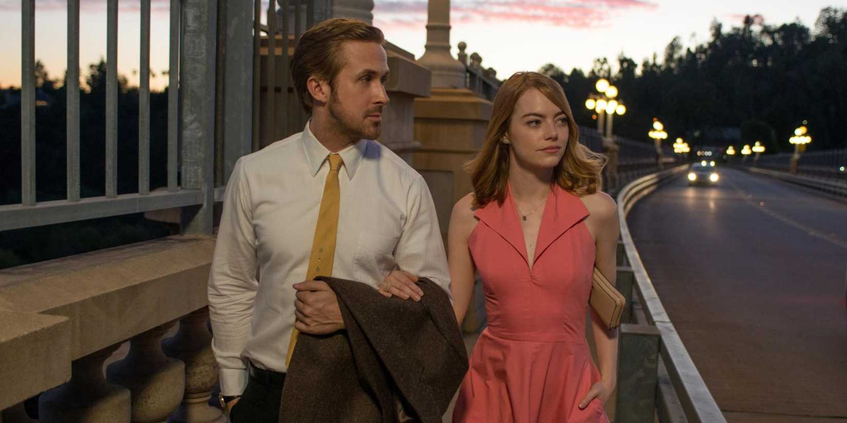 Emma Stone and Ryan Gosling walk by the side of a road arm in arm in La La Land.