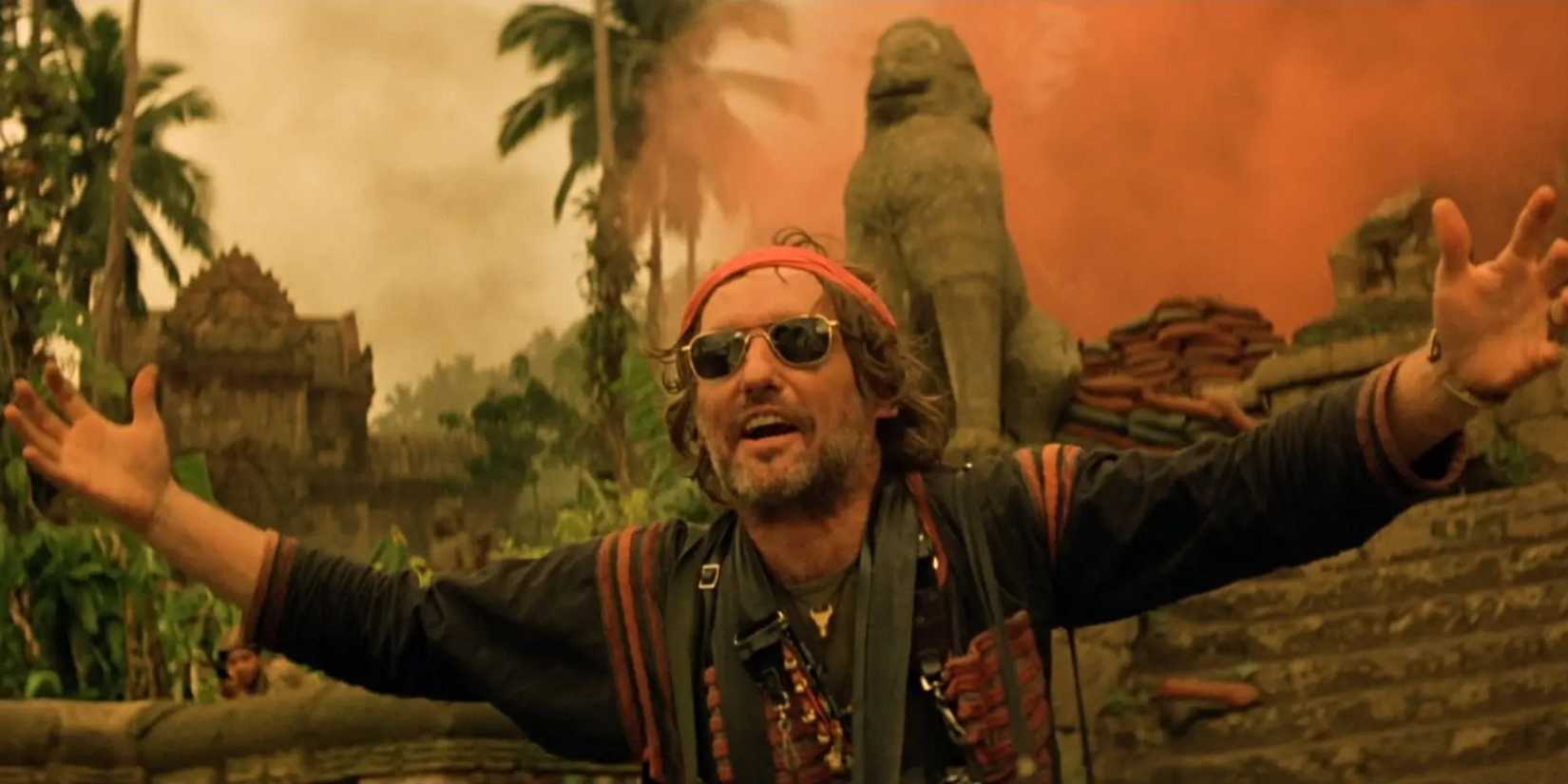Dennis Hopper as an American photojournalist, standing in front of a statue with his arms outstretched in Apocalypse Now