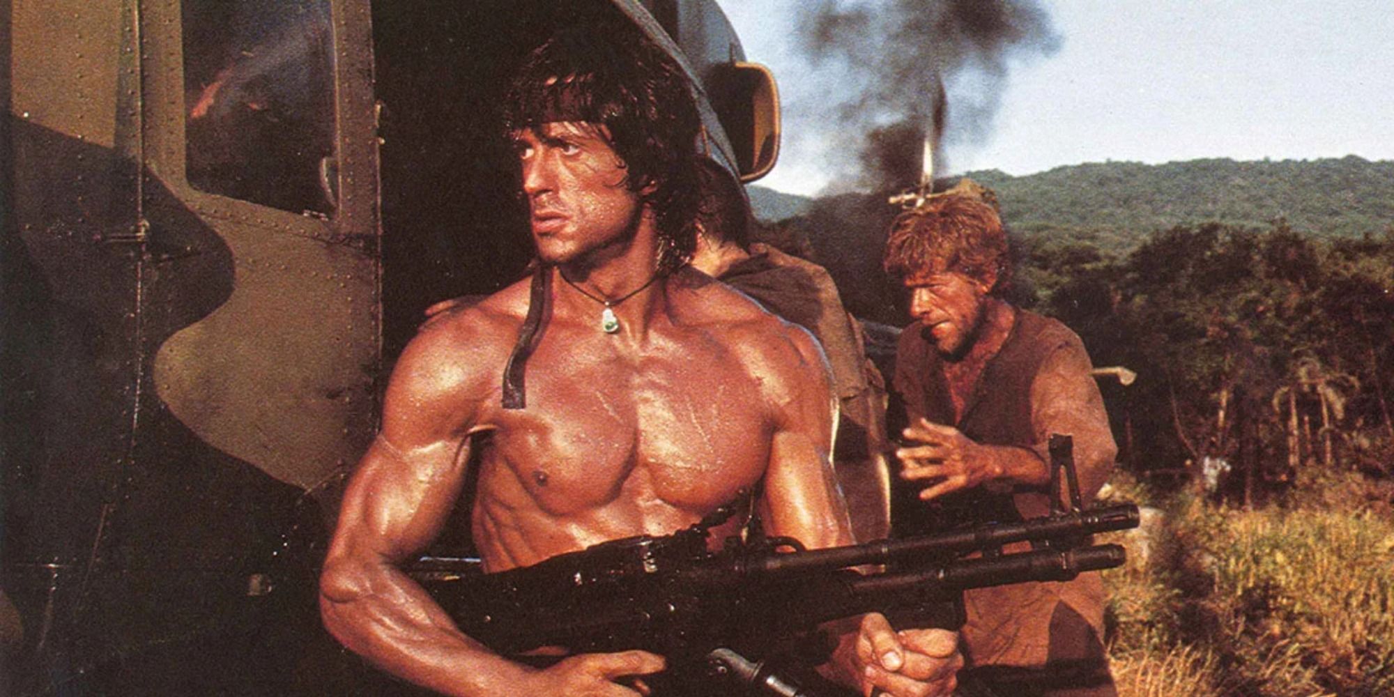 Sylvester Stallone as Rambo holding a gun beside a helicopter 