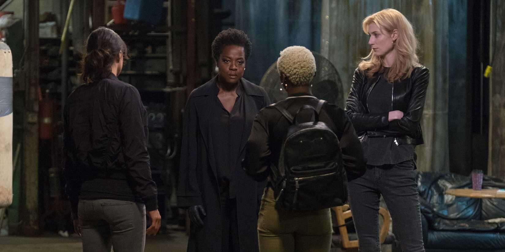 Four women have a serious conversation while standing in a rundown warehouse
