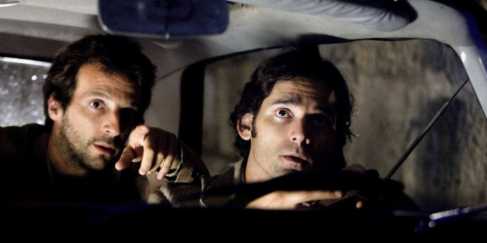 Avner and another man inside a car looking intently at something off-camera in Munich