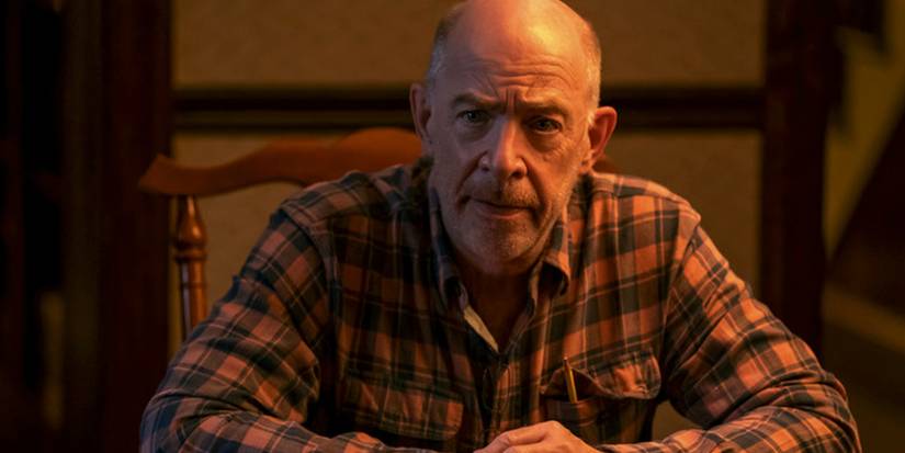 J.K. Simmons with a furrowed brow, sitting at a table and looking at someone off-screen in Night Sky