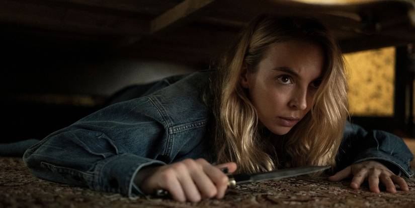 Villanelle from Killing Eve lying under something on the ground, holding a knife.