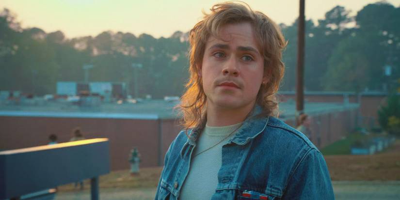 Dacre Montgomery as Billy in a denim jacket looking wistfully to the distance in Stranger Things.