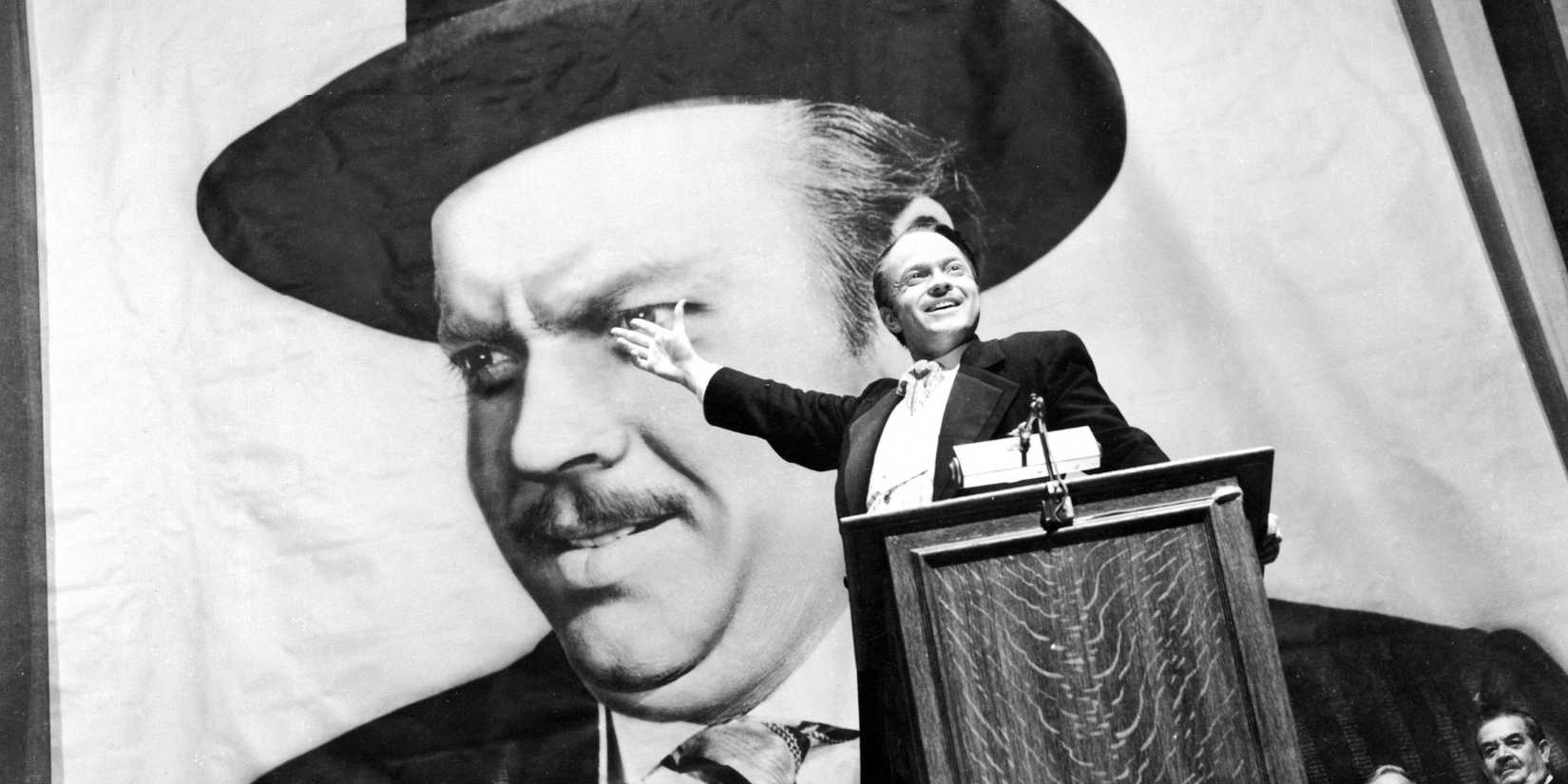 Charles Foster Kane, played by Orson Welles, stands in front of a massive poster of himself in Citizen Kane.