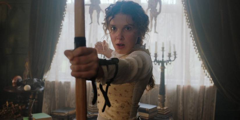 Enola Holmes aiming a bow and arrow at something beyond the screen in Enola Holmes