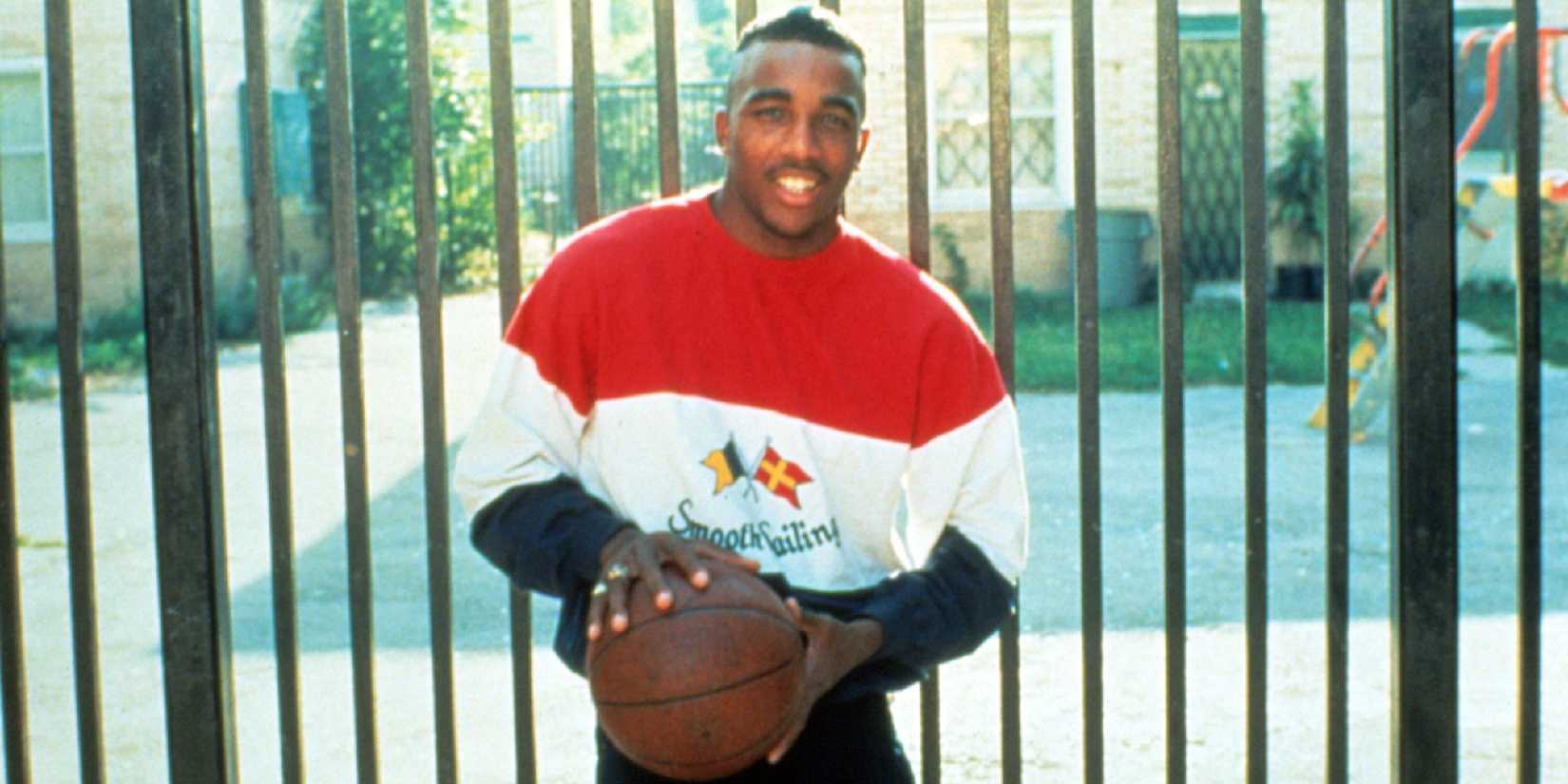 A man holds a basketball outside a fenced in yard in Hoop Dreams.