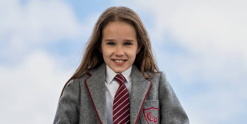 Matilda, played by Alisha Weir smiling for the camera in her school uniform in Matilda: The Musical.