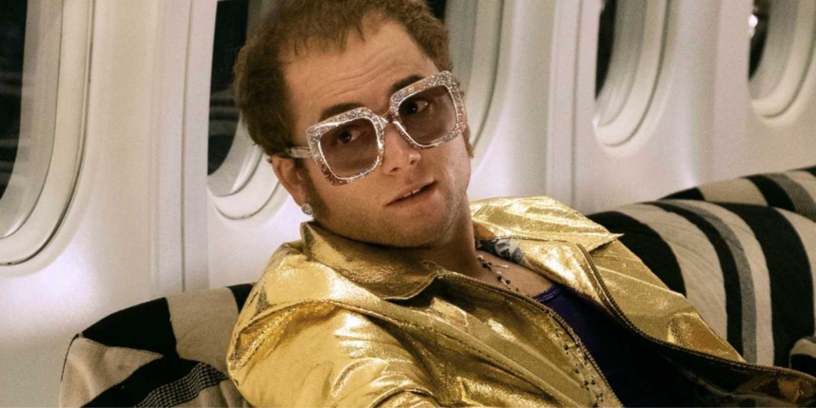 Elton John, played by actor Taron Egerton, on a private jet wearing a gold jacket and glasses in Rocketman.