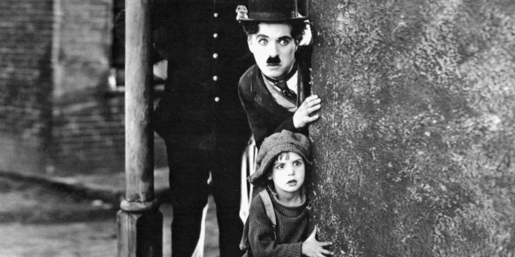 Charlie Chaplin and a young boy looking in the same direction from behind a wall corner in The Kid
