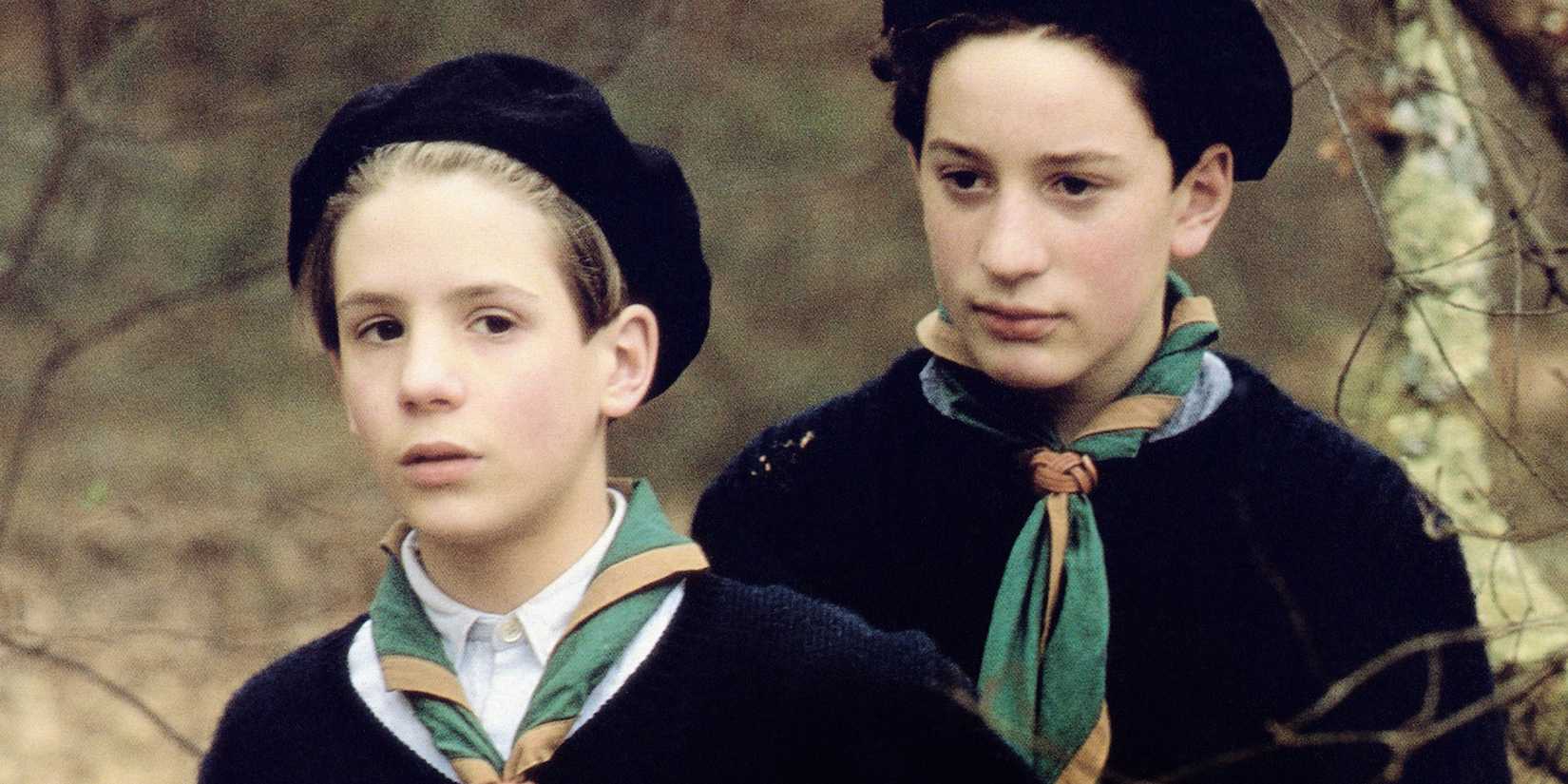 Two young boys wear matching outfits and walk through the woods in Au Revoir les Enfants.