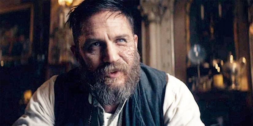 Tom Hardy di Peaky Blinders mencondongkan tubuh ke depan, berbicara, dengan bekas luka di sepanjang wajahnya