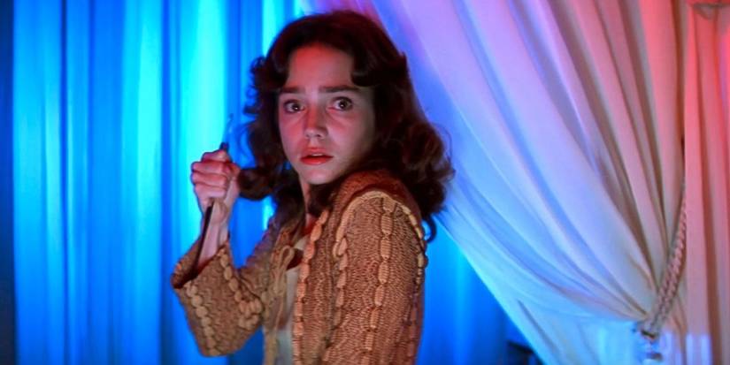 Suzy holds a knife and looks ahead in Suspiria.