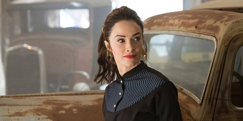 Abigail Spencer stands in front of an old car and wears a vintage dress in Timeless.
