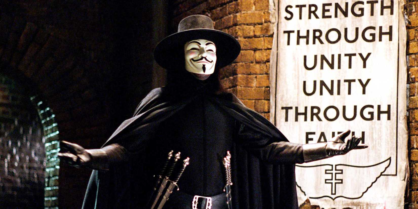 The masked vigilante V in an alleyway with a propaganda poster on the wall in V for Vendetta.